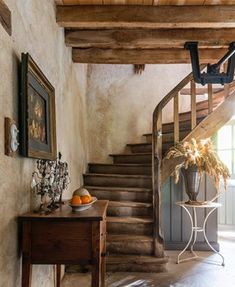 a wooden table sitting in front of a stair case next to a painting on the wall