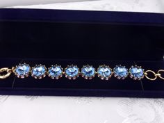 A truly eye-catching and elegant vintage piece in beautiful condition with an amazing sparkle! Beautiful and unique one-of-a kind design. The rhinestone bracelet is made up of eight blue topaz round cut faceted stones that measure 5/8", approximately the size of a dime. They are set in a goldtone metal surrounded at the base with small purple rhinestones.  The stones are securely set in a goldtone metal setting with no loose or missing stones. All have a brilliant sparkle! Will be packaged in a lovely blue velvet gift box as shown and ready for gift giving. For other vintage jewelry listings please visit:  https://www.etsy.com/shop/DreamofjeanieDesigns?ref=seller-platform-cnav&section_id=23284464 Jeweled Bracelets For Formal Occasions, Elegant Formal Topaz Bracelets, Elegant Formal Topaz Bracelet, Formal Jeweled Crystal Bracelets, Blue Round Crystal Bracelet For Formal Occasions, Blue Crystal Bracelet For Formal Occasions, Formal Blue Round Crystal Bracelet, Formal Crystal Bracelet With Stones, Costume Jewelry Bracelet With Sparkling Stones For Formal Occasions