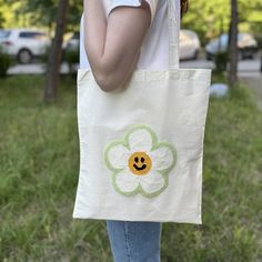 a person holding a white bag with a flower on it and a smiley face painted on the front