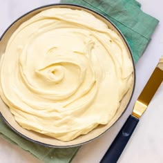 a pan filled with white frosting next to a knife and fork on top of a green napkin