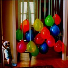 a little boy standing in front of a doorway with balloons hanging from it's ceiling