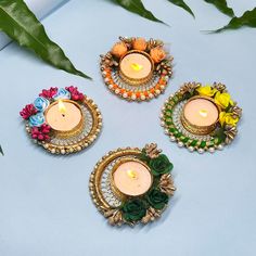 three small candles with flowers on them sitting next to some leaves and greenery in front of a blue background