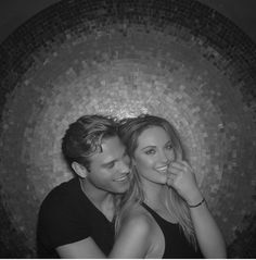 a man and woman posing for a photo in front of a mosaic wall with their arms around each other