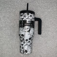 a black and white coffee cup with skulls on it sitting on a carpeted floor