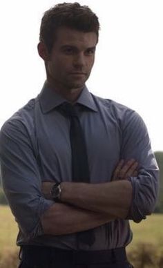 a man in a dress shirt and tie standing with his arms crossed