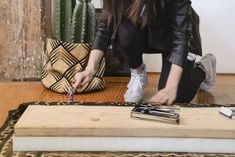 a woman kneeling down on the floor with her hand on top of a piece of wood