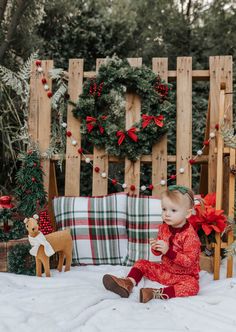 a toddler sitting on the snow in front of christmas wreaths and decorations, eating