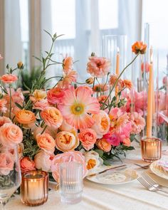 the table is set with pink and orange flowers, candles, and glass vases