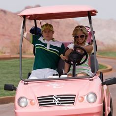 two people in a pink golf cart with the driver smiling and waving to the camera