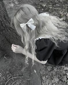 a woman with long blonde hair leaning against a tree wearing a black and white dress