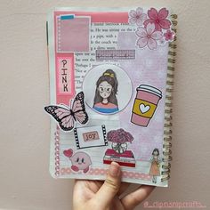 a hand holding up a small notebook with pictures and words on the pages, along with a cup of coffee