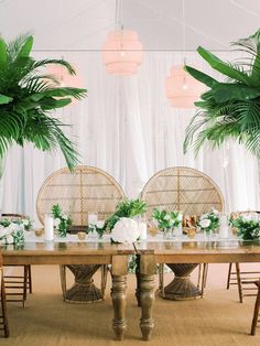 the table is set up with greenery and flowers on it, along with wicker chairs