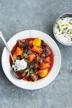 a white bowl filled with stew next to a small bowl of sour cream on the side