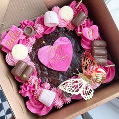 a heart shaped cake in a box decorated with pink and white flowers, chocolates, marshmallows