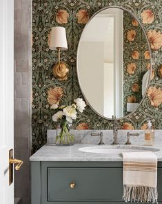 a bathroom vanity with a large mirror above it and flowers on the wall behind it