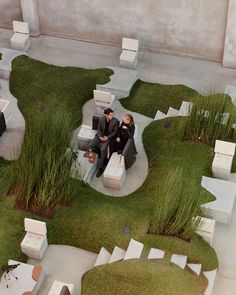 two men sitting on benches in the middle of a courtyard with grass growing all around them