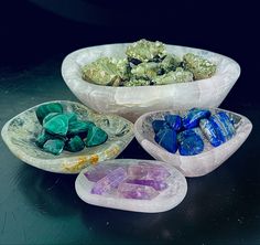 three bowls filled with different colored rocks on top of a black table next to each other