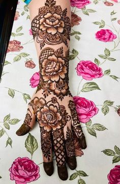 a woman's hand with henna on it and pink flowers in the background