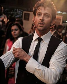 a man wearing a vest and tie standing in front of a group of other people