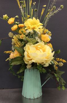 a blue vase filled with yellow flowers on top of a table next to a gray wall