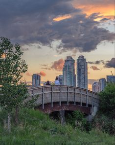 two people are standing on a bridge in front of the cityscape at sunset