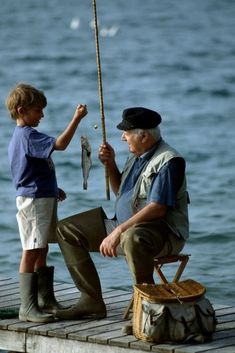 an old man sitting on a dock with a little boy holding a fish and fishing