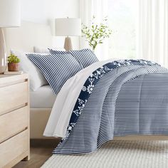 a bed with blue and white comforters in a bedroom next to a window,