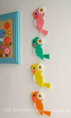 three colorful birds hanging on a wall next to a blue framed photo and a painting