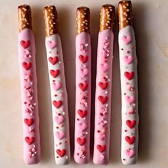 four pretzels decorated with hearts and sprinkles on a white surface