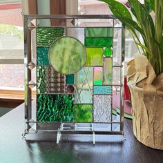 a vase filled with green plants next to a stained glass paneled window sill