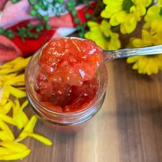 a spoon filled with jelly sitting on top of a wooden table next to yellow flowers