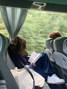 two people sitting on a bus looking out the window and reading books in their seats