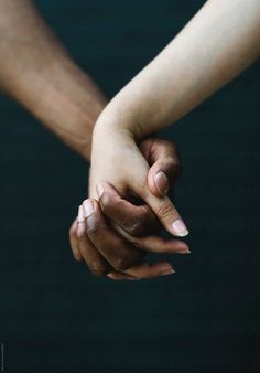 two people holding hands while standing next to each other in front of a dark background