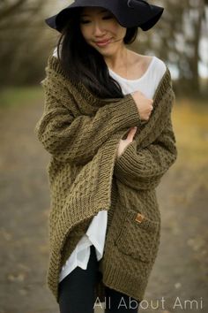 a woman wearing a black hat and green cardigan is posing for the camera with her hand on her hip