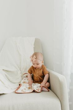 a baby is sitting on a couch reading a book