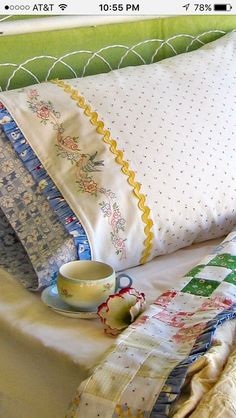 a bed topped with lots of pillows next to a cup and saucer