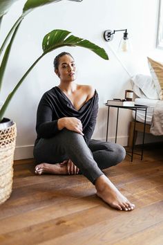 a woman sitting on the floor in front of a plant