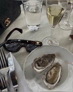 two oysters on a white plate with wine glasses and silverware next to it