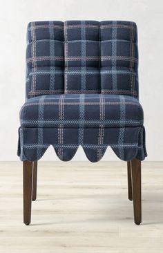 a blue plaid chair with scalloped legs on a wooden floor in front of a white wall