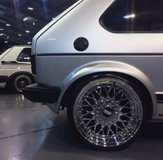 a silver car parked in a garage next to another white car with chrome rims