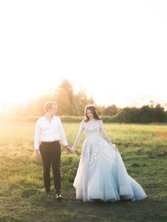 a bride and groom holding hands in a field at sunset with the sun behind them