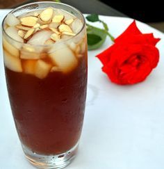 a glass filled with liquid and ice sitting next to a red rose on a table