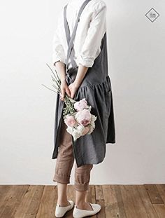 a woman standing in front of a white wall holding a bouquet of flowers and wearing an apron