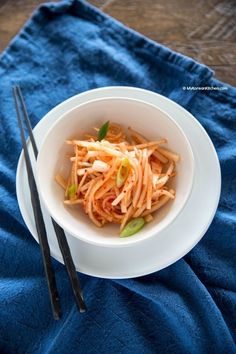 a white bowl filled with food on top of a blue towel next to chopsticks