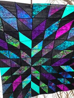 a black and purple quilt hanging from a clothes line with trees in the back ground