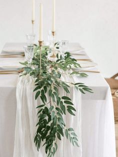 the table is set with white linens, candles and greenery for an elegant look