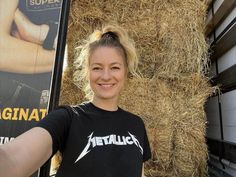 a woman standing in front of hay bales with her hand on her hip and smiling at the camera