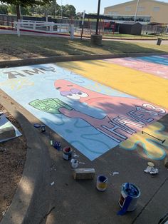 some paint cans are sitting on the ground in front of a large mural that says hello kitty