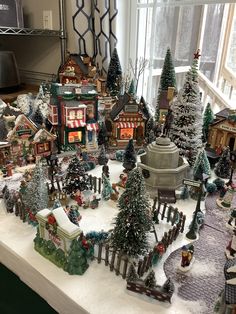 a christmas village is displayed on a table in front of a window with snow and trees