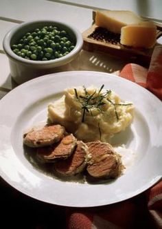 a white plate topped with meat and mashed potatoes next to two bowls of peas